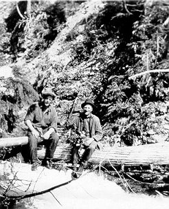 Men sitting on fallen tree stumps by a stream, wpH114